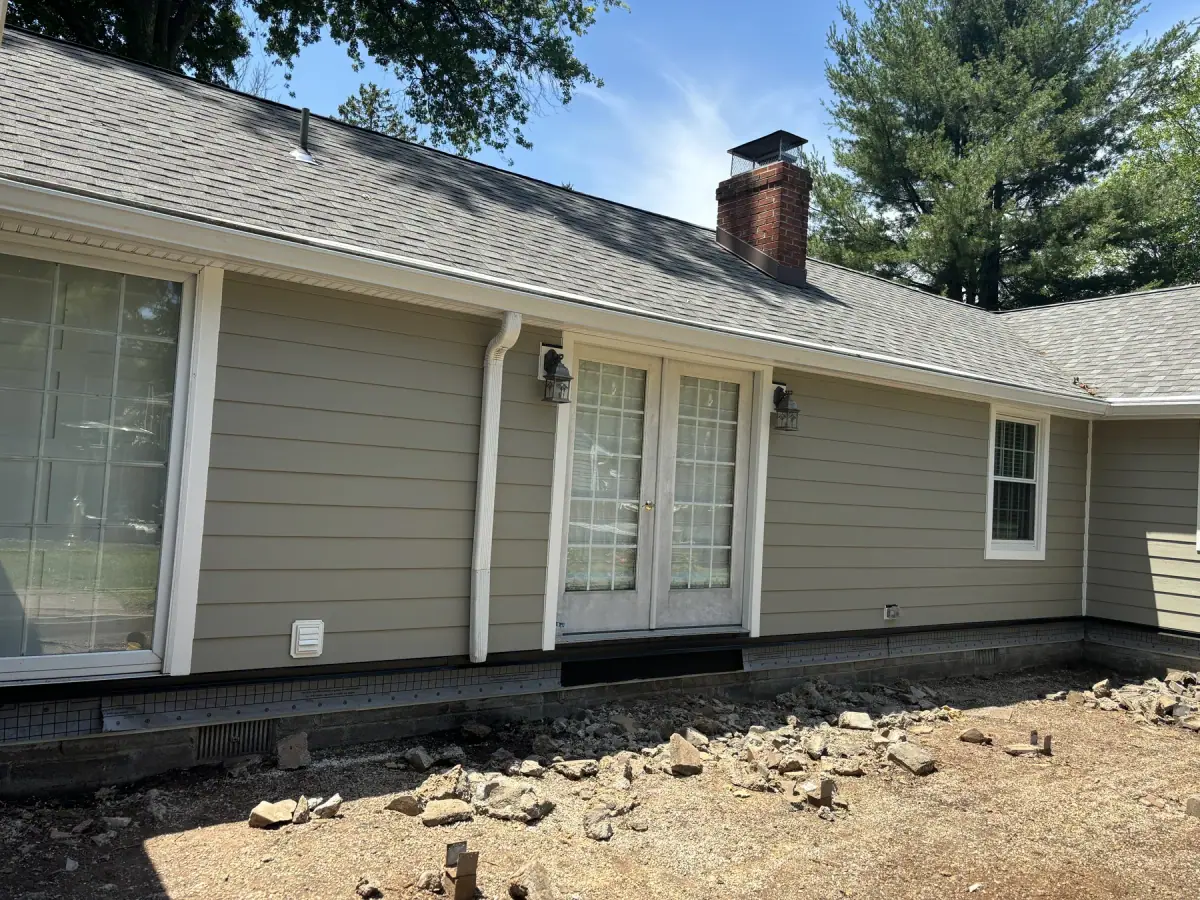 The long elevation of a ranch house in new sage green siding, brick chimney at the far end