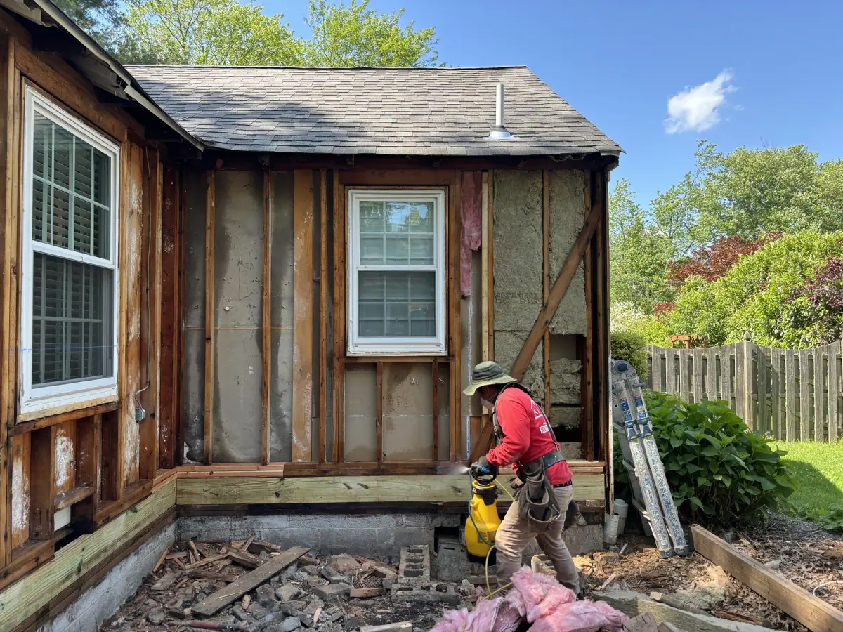A small house stripped back to bare studs and old sheathing, crew and debris in the garden