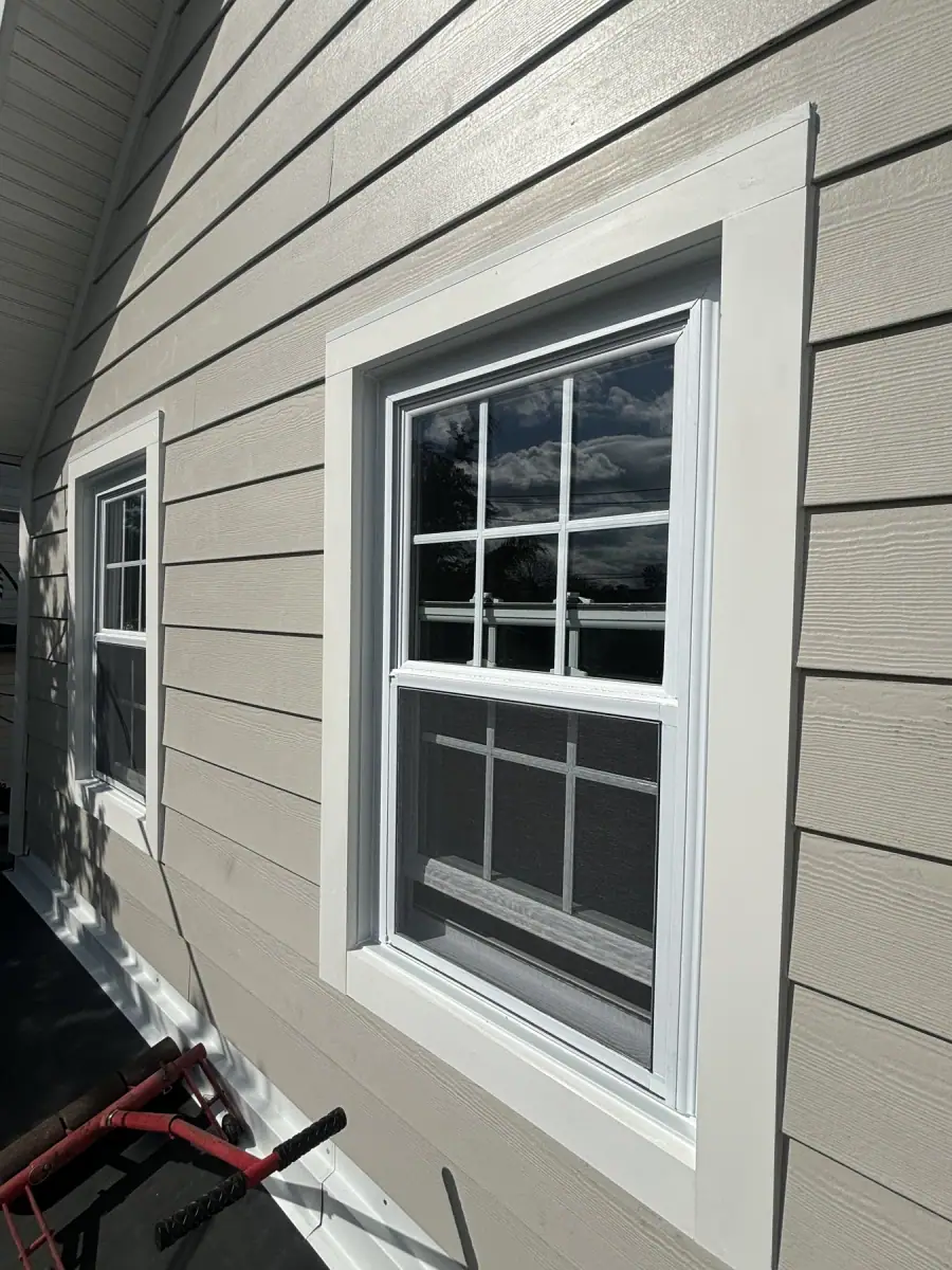 A window in new grey siding with the white trim boards finished tight around it